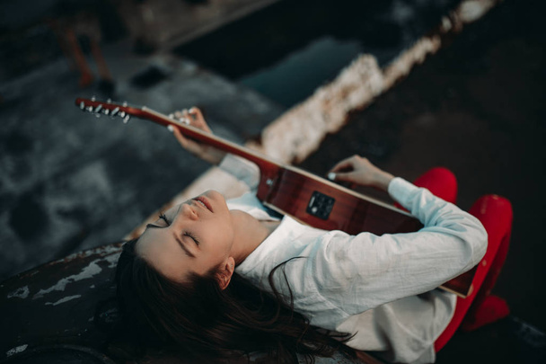 Nuori nainen makaa ja soittaa kitaraa hylätyllä laivalla.
. - Valokuva, kuva