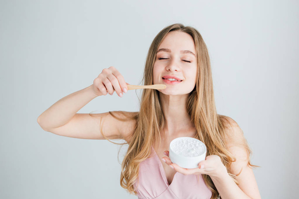 Girl holding a useful bamboo toothbrush and a jar of tooth powder - 写真・画像