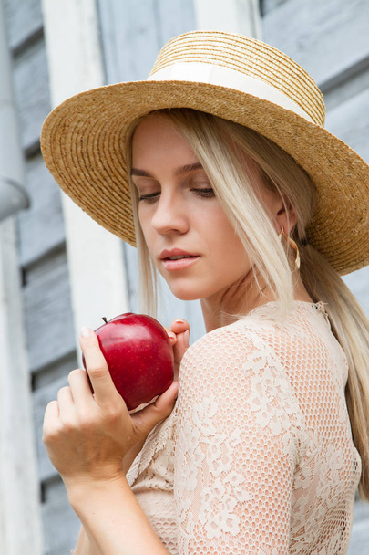 Το κορίτσι με το ψάθινο καπέλο κρατά ένα κόκκινο μήλο στα χέρια της - Φωτογραφία, εικόνα