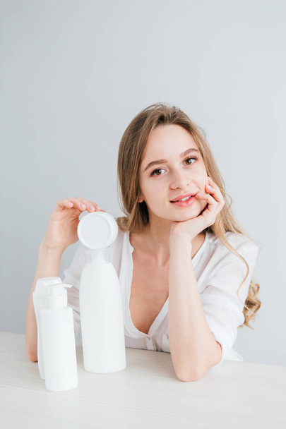 Young beautiful girl with white cosmetic bottles of different sizes - Foto, imagen