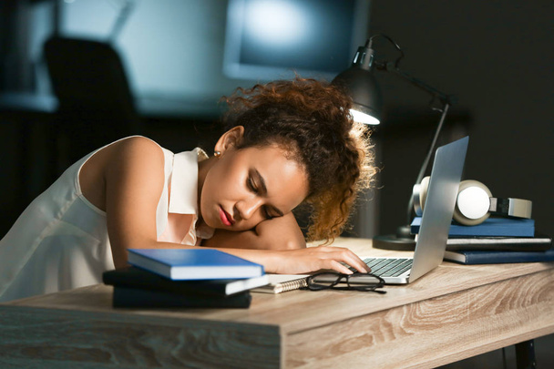 Tired African-American student sleeping at table instead of preparing for exam in evening - 写真・画像