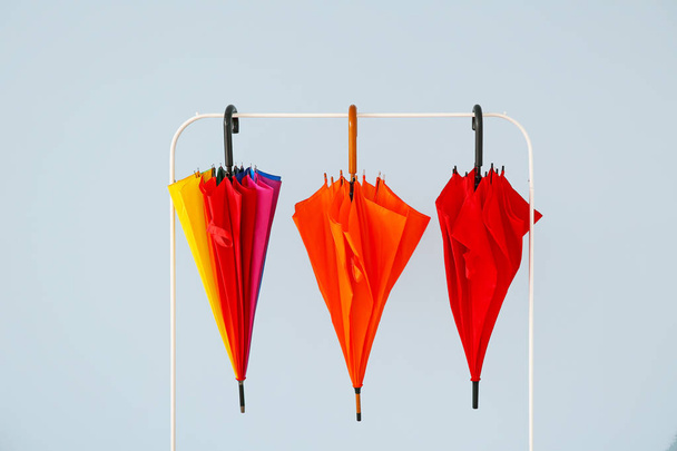Cremalheira de roupas com guarda-chuvas elegantes no fundo claro
 - Foto, Imagem