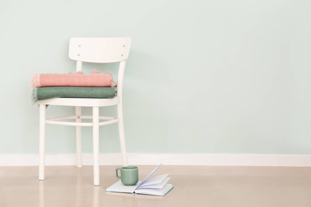 Chair with plaids and book with cup on floor near light wall - Photo, Image