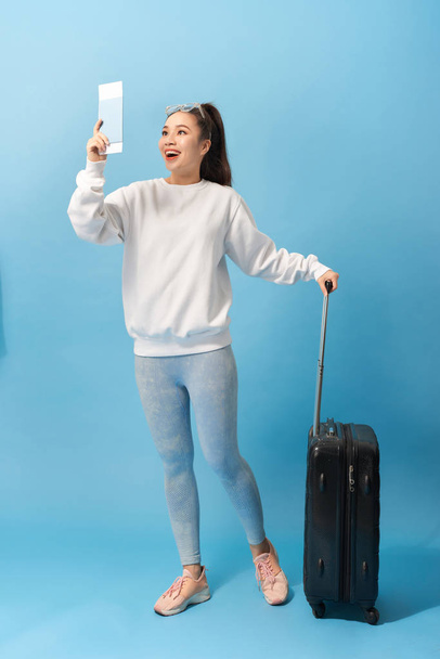 Turystyka, urlop letni i koncepcja urlopowa-szczęśliwa Kobieta w nieformalnej odzieży z torbą podróżną i biletem lotniczym na niebieskim tle - Zdjęcie, obraz