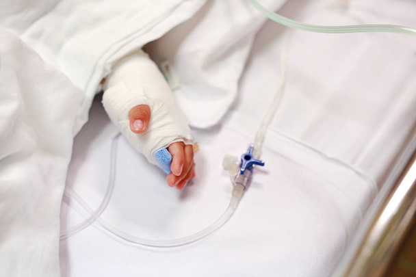 Close up baby hand on patient's bed in hospital with saline intravenous. Baby admitted at hospital. Kid patients have IV tube. - Foto, afbeelding