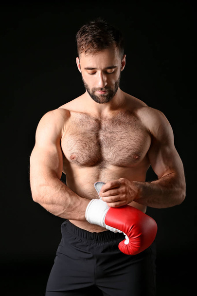 Strong male boxer putting on gloves against dark background - Фото, зображення