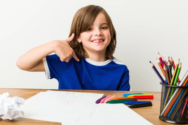 Niño pequeño pintando y haciendo deberes en su escritorio persona señalando a mano a un espacio de copia de la camisa, orgulloso y confiado
 - Foto, Imagen
