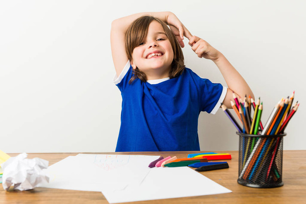 Маленький мальчик рисует и делает домашние работы на столе растягивая руки, расслабленное положение
. - Фото, изображение