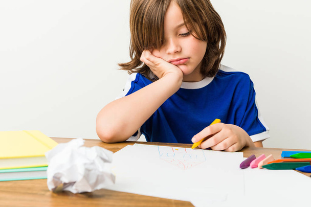 Niño pequeño pintando y haciendo deberes en su escritorio que está aburrido, fatigado y necesita un día de relax
. - Foto, Imagen