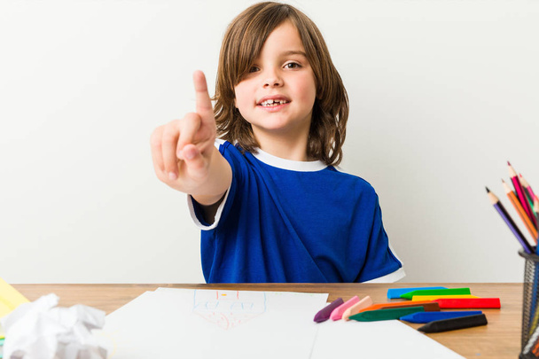 Niño pintando y haciendo deberes en su escritorio mostrando el número uno con el dedo
. - Foto, Imagen