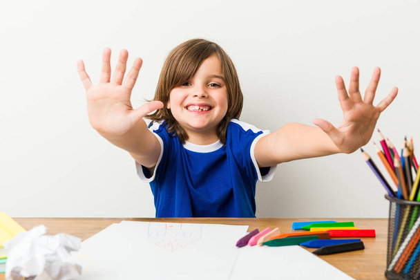 Niño pintando y haciendo deberes en su escritorio mostrando el número diez con las manos
. - Foto, Imagen