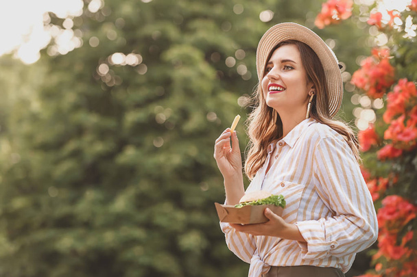 Красивая молодая женщина ест вкусную картошку фри на открытом воздухе
 - Фото, изображение