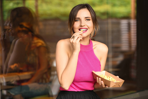 Красивая молодая женщина ест вкусную картошку фри на открытом воздухе кафе
 - Фото, изображение