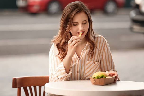 Belle jeune femme mangeant de savoureuses frites dans un café extérieur
 - Photo, image