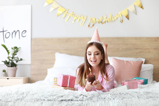 Femme heureuse avec gâteau d'anniversaire couché sur le lit à la maison
 - Photo, image