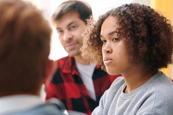 Serieuze mixed-race meisje kijkend naar een van groupmates terwijl het luisteren naar zijn uitleg tijdens de les - Foto, afbeelding