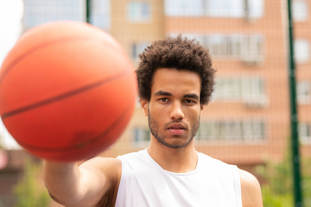 Young serious basketball player looking at you while passing ball or going to throw it in basket - Photo, image