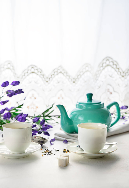 緑茶付き白茶カップ2杯、ティール色のティーポット、コピースペース付きの白い背景に紫色の花 - 写真・画像