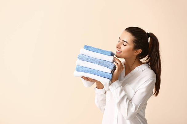 Beautiful young woman with stack of clean towels on light background - Фото, зображення