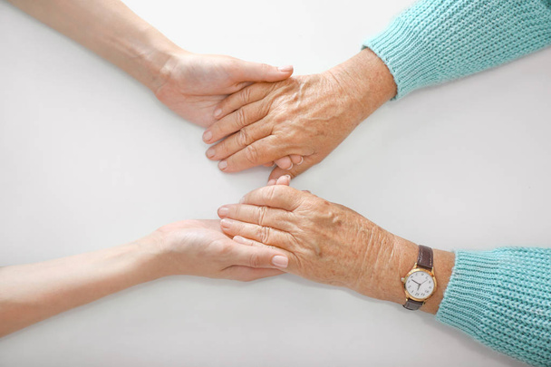 Руки молодой и пожилой женщины на белом фоне. Концепция поддержки
 - Фото, изображение
