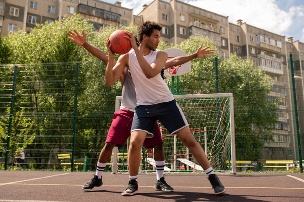 Один из баскетболистов с мячом старается не позволить сопернику забрать его во время игры на открытом воздухе
 - Фото, изображение