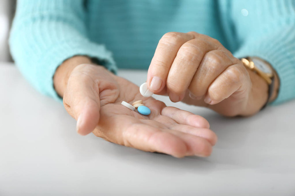 Oudere vrouw met pillen aan witte tafel, close-up - Foto, afbeelding