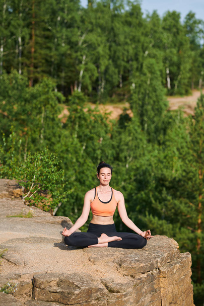 山の中で足を組んで座り、静かに瞑想を実践する目を閉じた平和な若い女性 - 写真・画像