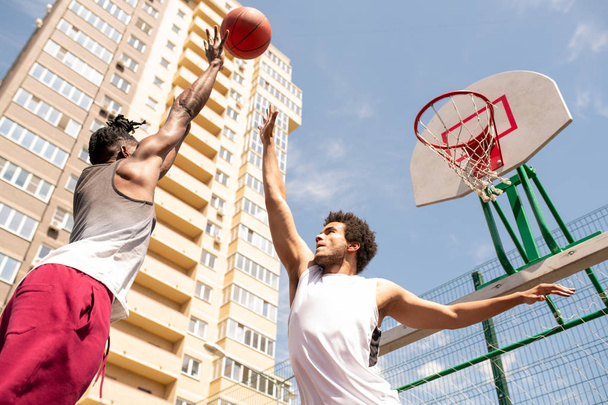 ボールをキャッチしようとするアクティブウェアの2人の若いプロの異文化バスケットボール選手 - 写真・画像