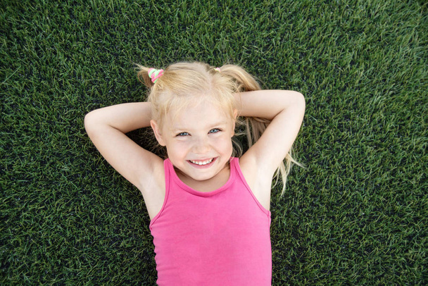 Πορτρέτο ενός χαμογελαστού κοριτσιού ξαπλωμένο στο πράσινο γρασίδι - Φωτογραφία, εικόνα