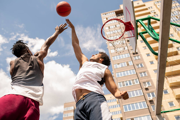 屋外のバスケットボールの試合中にボールをキャッチしようとしているスポーツウェアの若いアクティブな選手 - 写真・画像