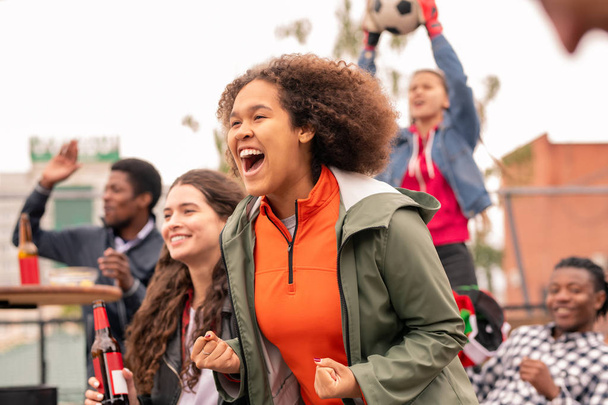 Chica de raza mixta extática y sus amigos interculturales animando a su equipo de fútbol después de gol
 - Foto, imagen