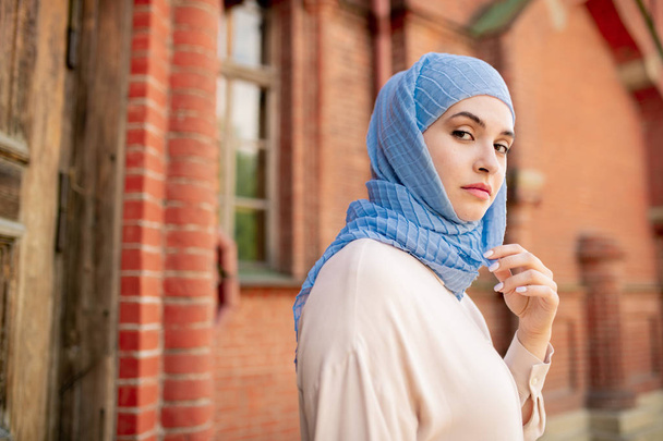 Молодий серйозний Арабська жінка в блакитному хіджаб дивлячись на вас, приймаючи ходити по стародавньому храмі - Фото, зображення