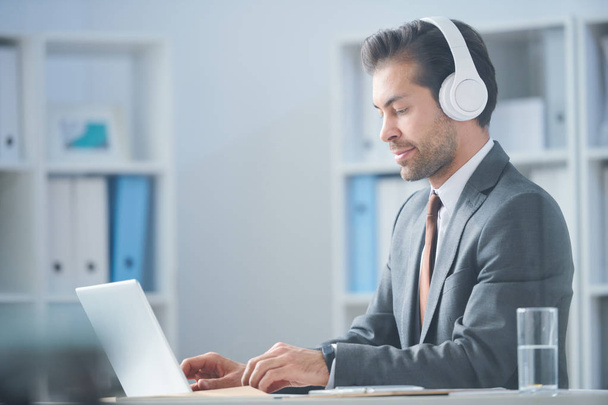 junger seriöser Geschäftsmann mit Kopfhörer schaut sich Online-Video über neue Geschäftstrends an - Foto, Bild