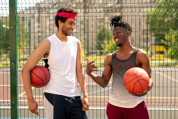 Dwóch młodych towarzyskich towarzysze koszykówki dyskusji kilka ciekawych chwil gry stojąc przez ogrodzenie placu zabaw - Zdjęcie, obraz