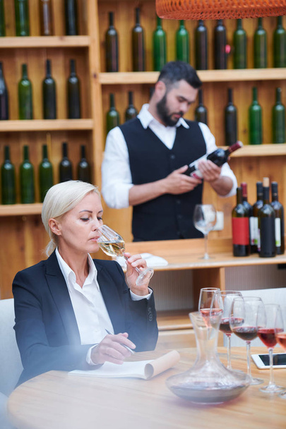 Jolie cave expert dégustation vin blanc de verre à vin et de mettre ses caractéristiques dans le bloc-notes
 - Photo, image