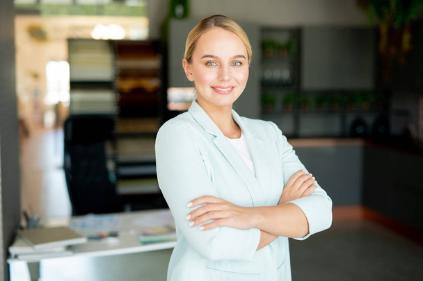 Молодая уверенная в себе бизнес-лидер в формальной одежде смотрит на тебя, стоя в своем офисе
 - Фото, изображение