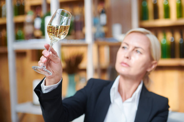 Женщина держит в руках бокал белого вина при изучении его цвета и других характеристик
 - Фото, изображение