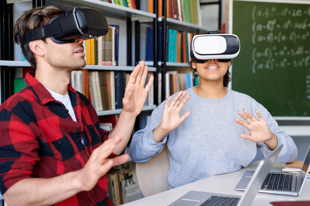 Νέοι έκπληκτος άντρας και γυναίκα σε VR ακουστικά με εικονική εμπειρία στο μάθημα στο κολλέγιο - Φωτογραφία, εικόνα