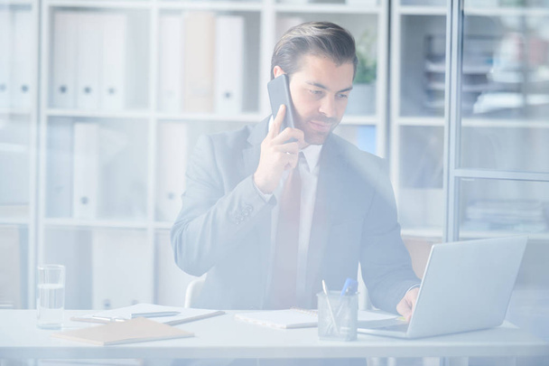 Beschäftigter junger Agent in Formalwear berät Kunden am Telefon und online während der Arbeit im Büro - Foto, Bild