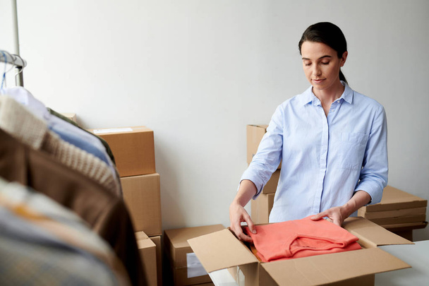 Молодий випадковий працівник кладе складений повсякденний одяг в коробку в процесі упаковки замовлення клієнта в офіс
 - Фото, зображення