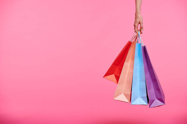 Mão de comprador segurando um monte de sacos de papel coloridos ou carregando-os depois de fazer compras em fundo rosa
 - Foto, Imagem