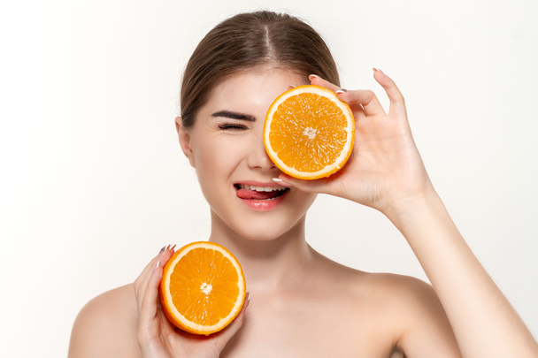 白い背景の上に孤立した顔に近いオレンジの半分を保持する幸せな美しい若い女の子のクローズアップ肖像画. - 写真・画像