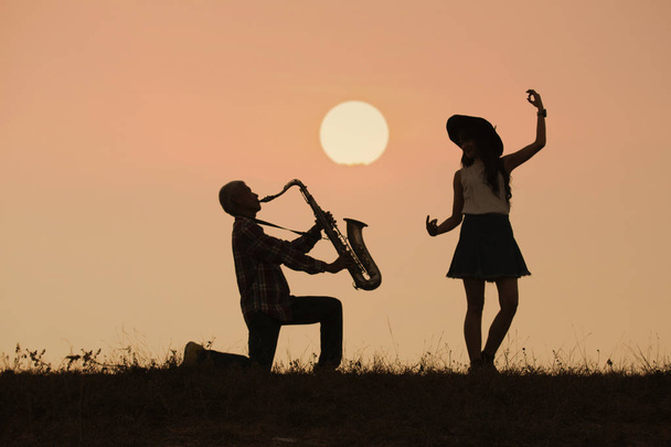 muusikko soittaa saksofonia auringonlaskun tai auringonnousun taustalla
 - Valokuva, kuva