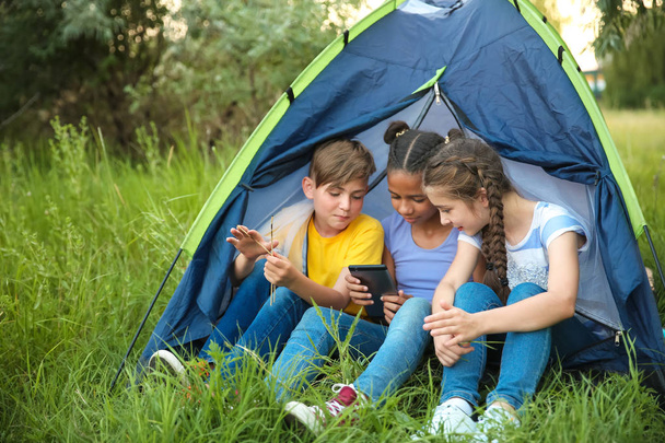 Niños con teléfono móvil sentados cerca de la tienda en el campamento de verano
 - Foto, Imagen
