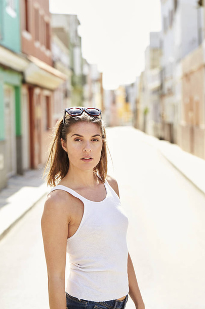 Beautiful girl in white vest standing in sunlit street, portrait - Фото, зображення