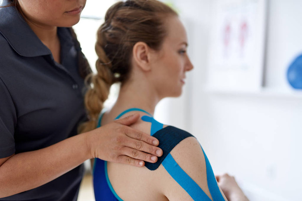 Chinese woman massage therapist applying kinesio tape to the shoulders and neck of an attractive blond client in a bright medical office - Valokuva, kuva