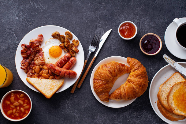 Classical english breakfast with fried bacon and mushrooms with eggs served with croissants and black coffee on grey background - Foto, immagini