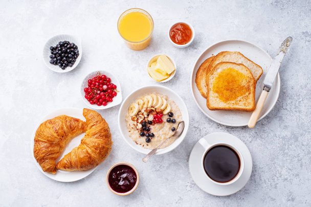 Desayuno con harina de avena y bayas con croissants y tostadas en la mesa
  - Foto, imagen