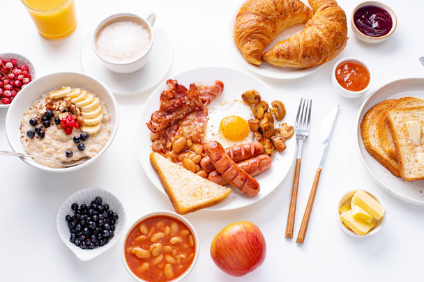 smažená vejce se slaninou a uzenky s ovesnou moučkou a bobule, smažené toasty a marmelády na bílém pozadí  - Fotografie, Obrázek