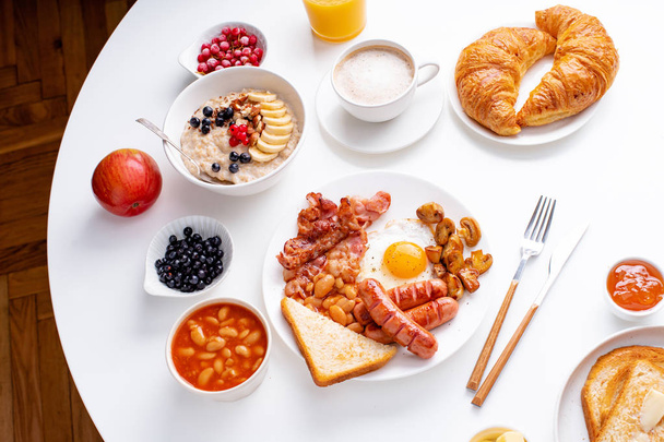 fried eggs with bacon and sausages with oatmeal and berries with fried toasts and jam on white background  - Foto, immagini